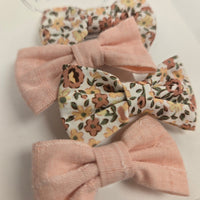 Four fabric hair bows, two floral and two solid pink, on a light background.