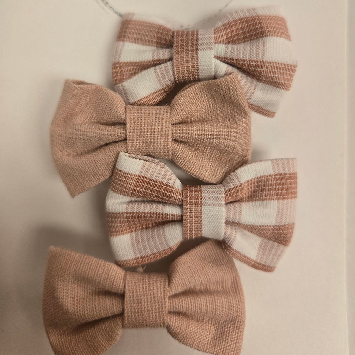 Four fabric bows with plaid patterns on a white background with complementary pink clips